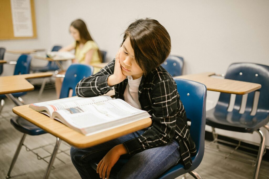 A young student absorbed in reading a book in an educational classroom environment.